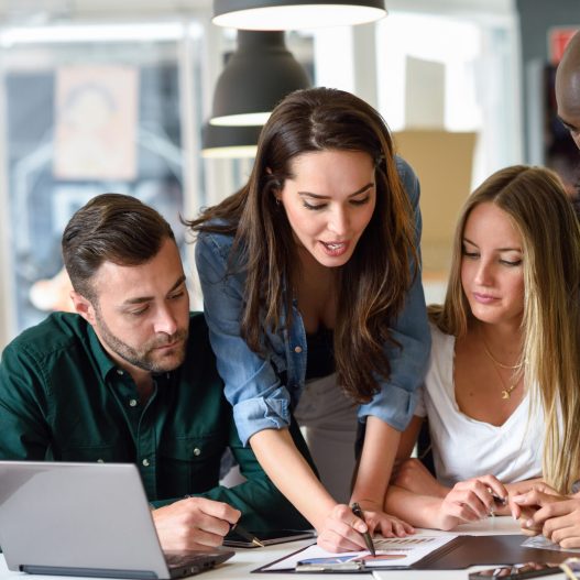 Five young people studying on white desk. Beautiful women and men working together wearing casual clothes. Multi-ethnic group.